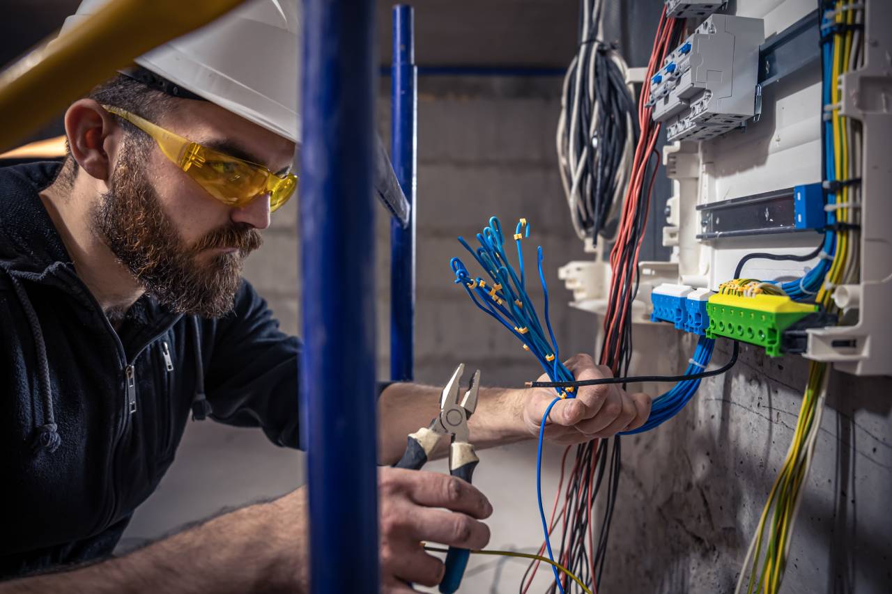 A Man Wearing A White Hard Hat And Safety Goggles, Working On Electrical Wiring In A Room